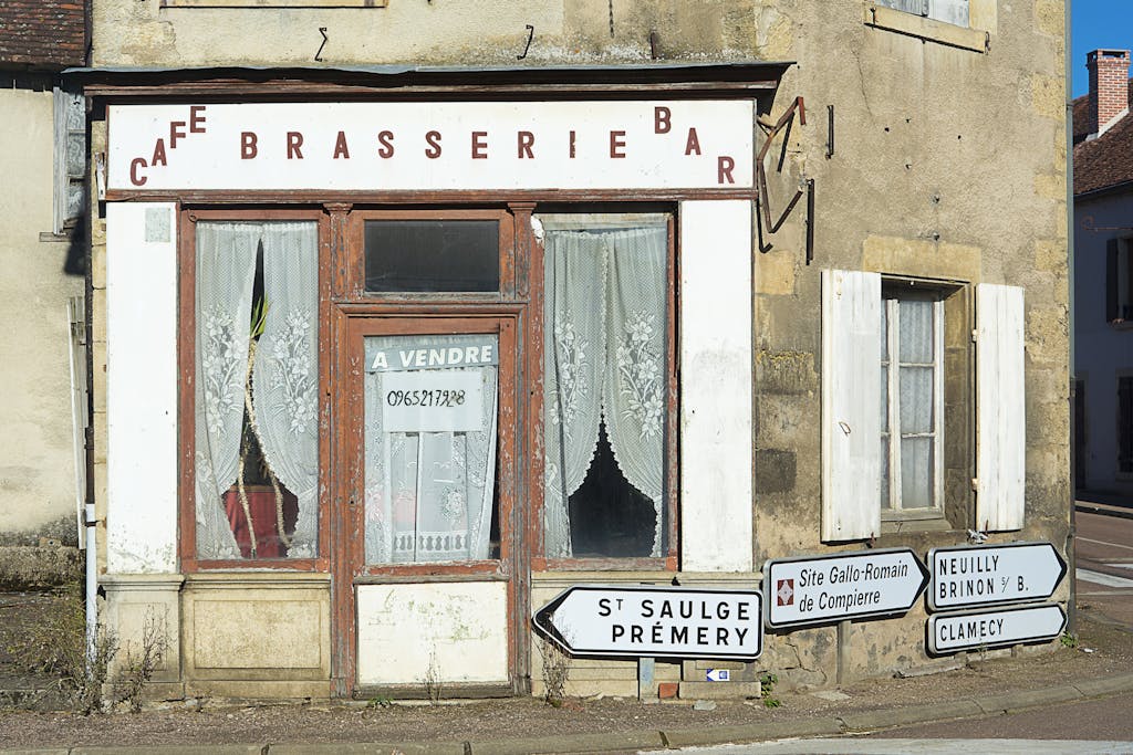 A deserted French cafe brasserie with a for sale sign in a small town setting.