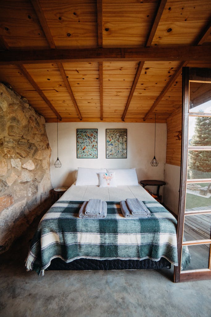 A warm and inviting rustic bedroom with stone wall and plaid blanket, ideal for a countryside retreat.