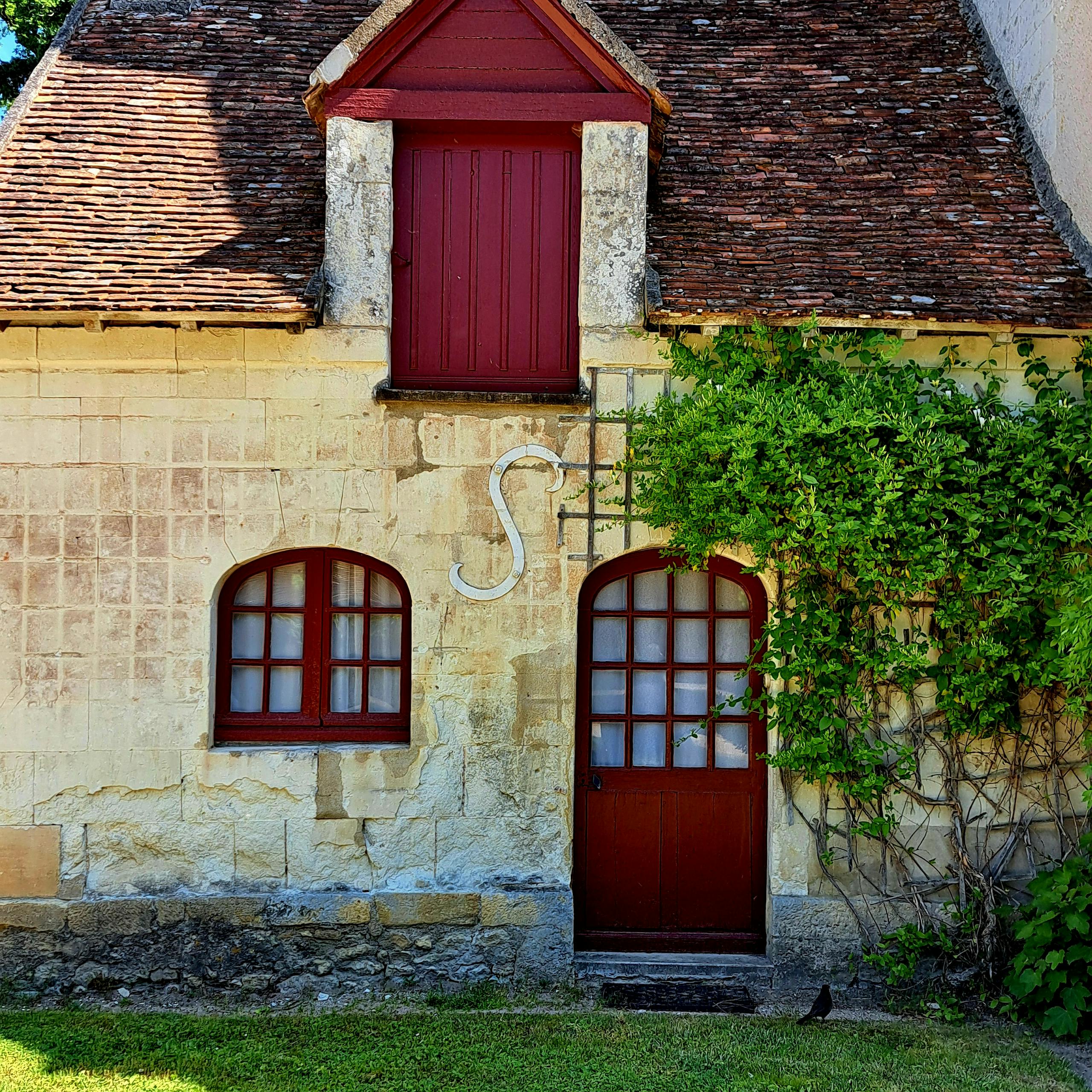 Rustic cottage facade with red accents, ivy, and arched windows, creating a quaint and charming atmosphere.